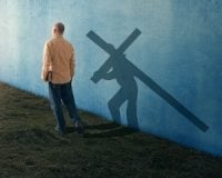 A man walking with his shadow carrying the cross