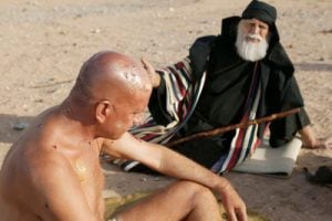 Naked man in desert sitting with friend