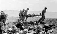 U.S. Corpsmen carry a wounded Marine on a stretcher to an evacuation boat on the beach at Iwo Jima while other Marines huddle in a foxhole during the invasion of the Japanese Volcano Island stronghold in this file photo of Feb. 25, 1945.