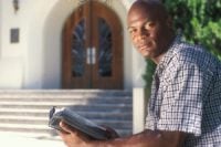 Black man holding Bible in front of church.