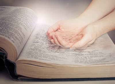 Woman\'s hands cupping water out of the pages of the Bible.