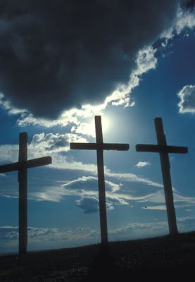Three crosses silhouetted by blue sky and clouds.